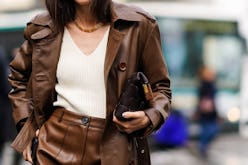 A woman walking in a brown coat, white shirt, and brown skirt down a street