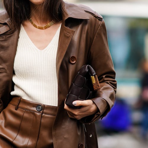 A woman walking in a brown coat, white shirt, and brown skirt down a street