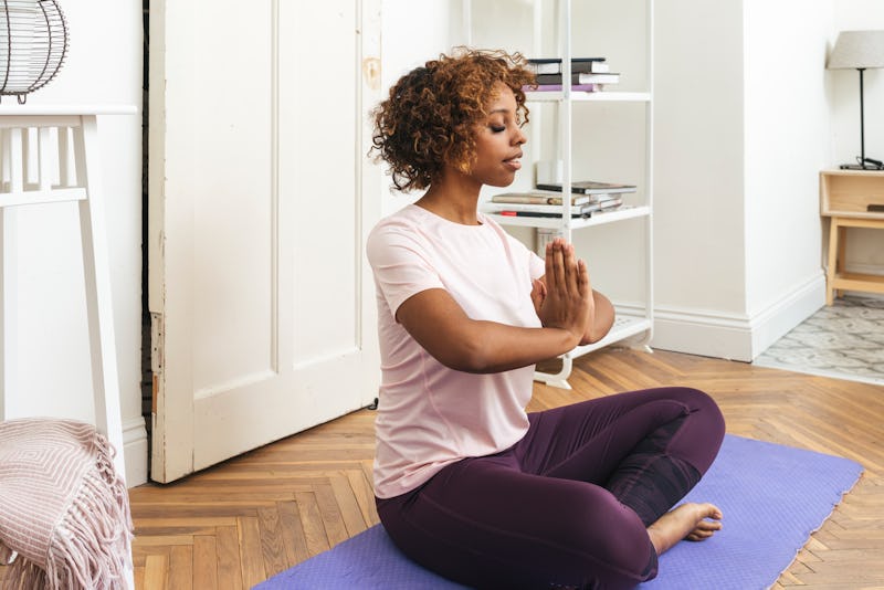 A woman sits with her hands in prayer pose before doing a yoga youtube video for when you don't feel...