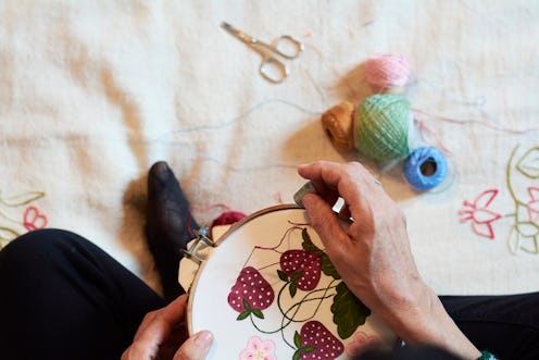 A woman embroiders strawberries onto plain fabric. These 9 DIY projects help when you're sad and nee...