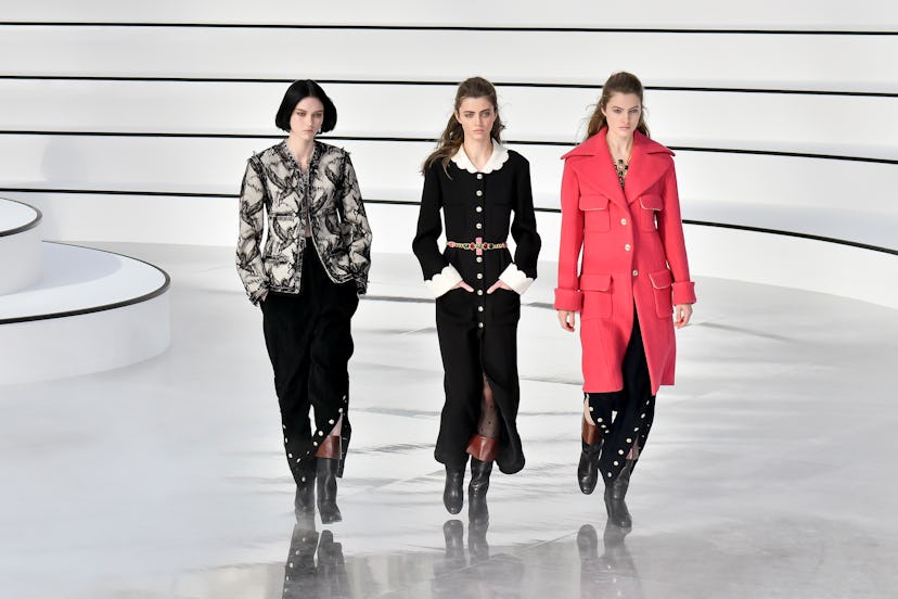 Three models on a runway at Chanel's Fall 2020 show sporting a floral jacket, black-and-white dress,...