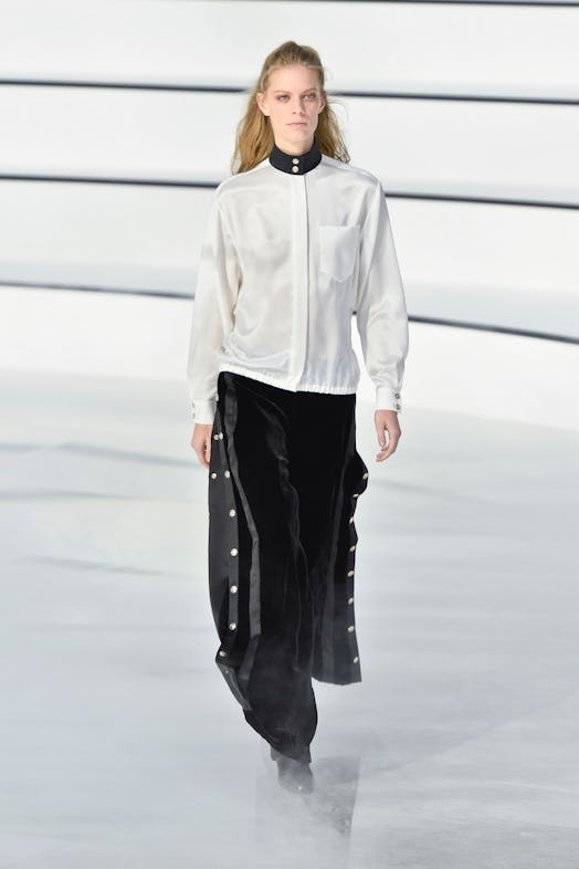 A model on a runway at Chanel's Fall 2020 show wearing a white jacket with a black collar, and black...