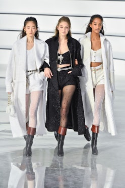 Two models in white coats, white shorts, and tops and a model in a black coat, black shorts and top ...