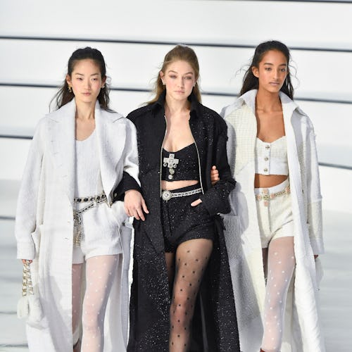 Two models in white coats, white shorts, and tops and a model in a black coat, black shorts and top ...