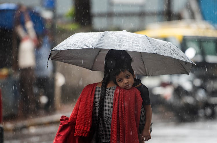 A mom in India carries her little boy through the rain.