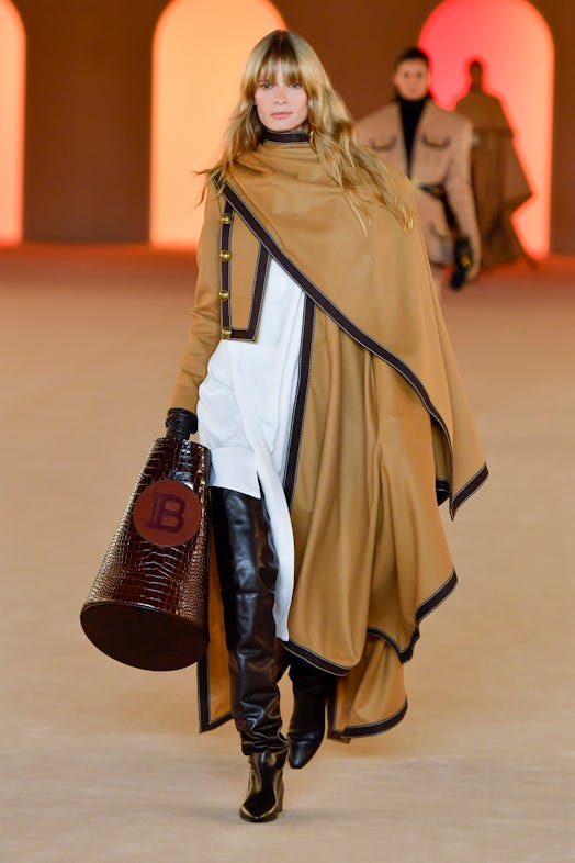 A model walking the runway in a floor-length camel cape, a white shirt and black leather pants