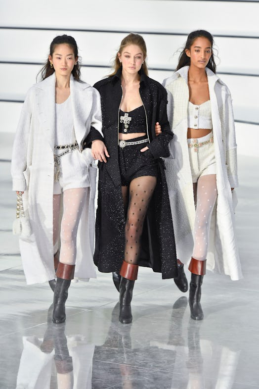 Three models walking the runway in high-waisted shorts, sheer tights, and duster coats by Chanel
