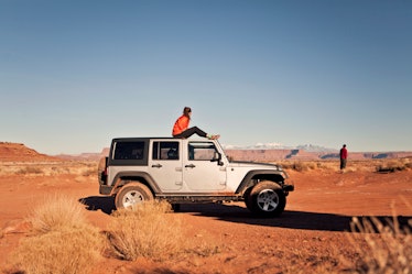 A woman sits on a white jeep in the middle of Canyonlands National Park.
