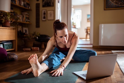 A young woman stretches on her yoga mat while following along with an at-home workout.