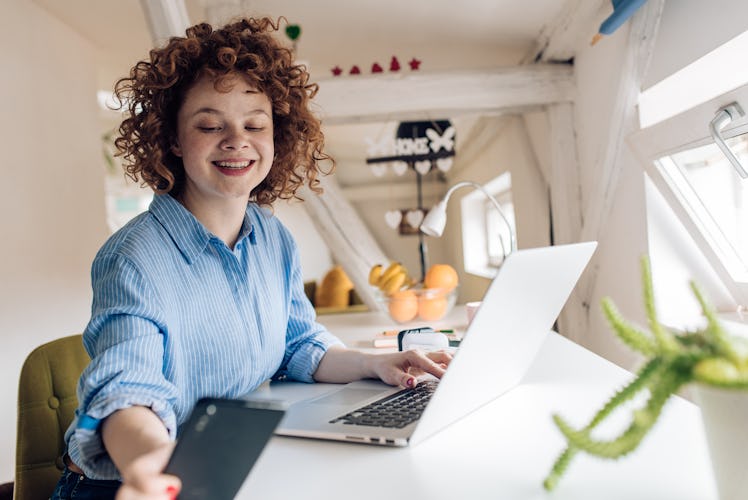 A woman wearing a striped blue and white button down looks at her phone and smiles while sitting at ...