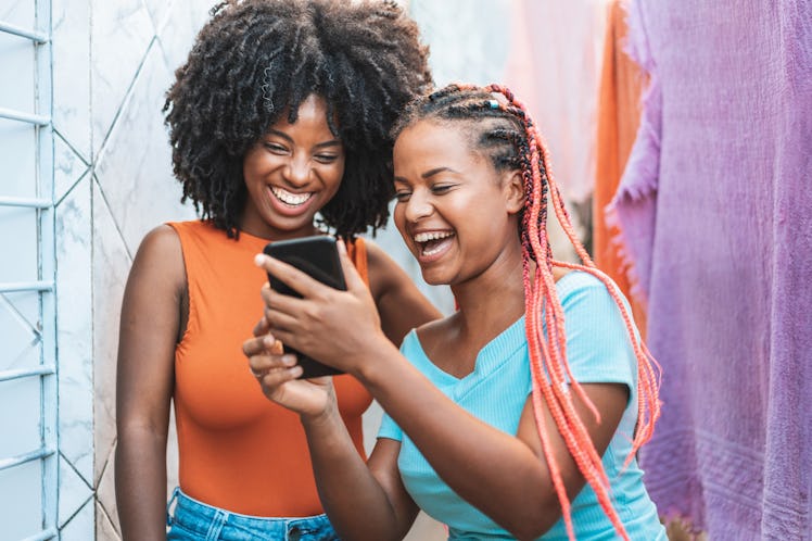 Two best friends video chat on their phone while standing outdoors near colorful towels.