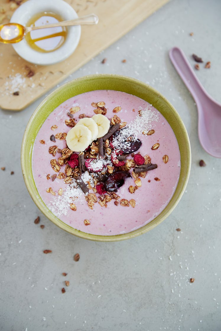 A pink smoothie bowl is prepared on a kitchen counter, and is filled with banana slices and granola.