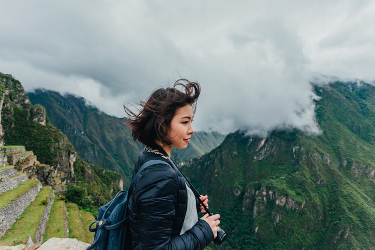 A young woman stands in front of Machu Picchu in Peru with a camera around her neck.