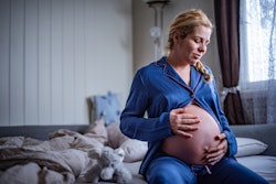 Pregnant woman in third trimester sitting on edge of bed, feeling baby's movement