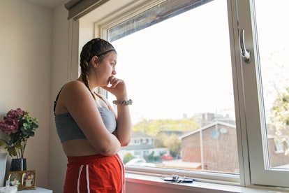 A person wearing red shorts and a sports bra stares out the bedroom window. Creating a new normal wh...