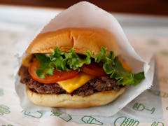 A Shake Shack burger sits on a tray with lettuce, tomato, and cheese, wrapped in paper. 