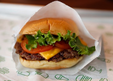 A Shake Shack burger sits on a tray with lettuce, tomato, and cheese, wrapped in paper. 