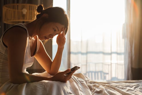 A woman looks at her phone with a headache. Stress, confinement and remote working may be causing gr...