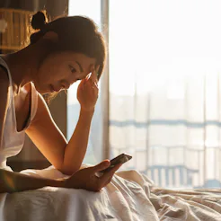 A woman looks at her phone with a headache. Stress, confinement and remote working may be causing gr...