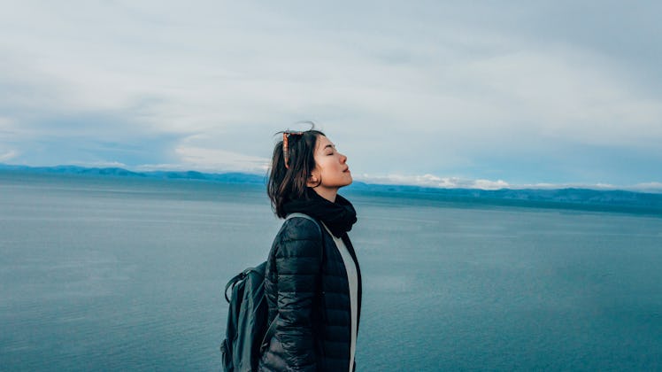 A young woman peacefully stands in front of an ocean.