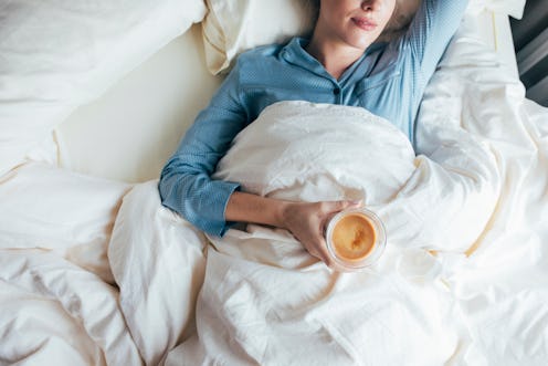A woman drinks coffee in bed. We asked doctors about ways not having sex for a long time can affect ...