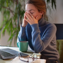 A woman rubs here eyes while on her computer. Coronavirus quarantine and increased screen time may b...