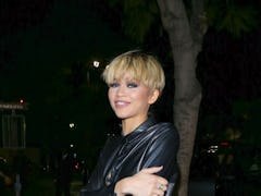 Zendaya stands with folded arms in a leather shirt with her hair cut into a short, pixie bowl cut, o...
