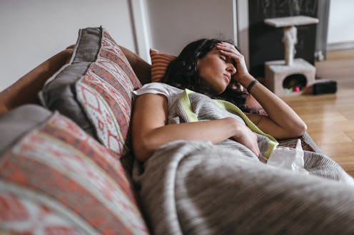A woman lies on a multicolor couch during a PMDD flare up during the coronavirus pandemic.
