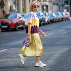 Young lady in satin yellow dress and white shoes crosses the street