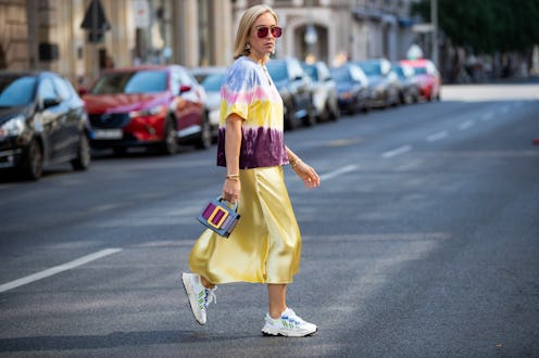 Young lady in satin yellow dress and white shoes crosses the street