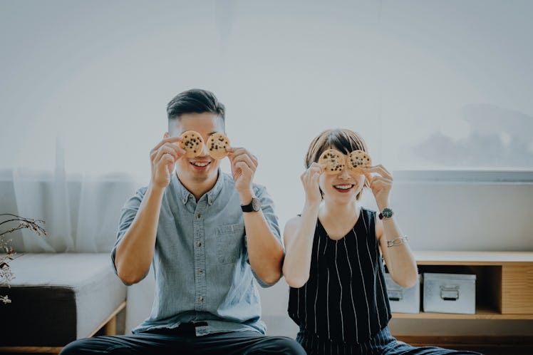 A young couple poses with chocolate chip cookies over their eyes.
