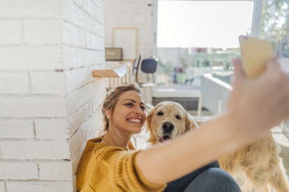 A young woman in a yellow sweater takes a selfie with her golden retriever.