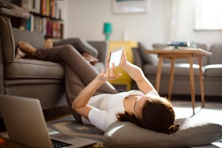 woman lying down in living room, looking at her phone