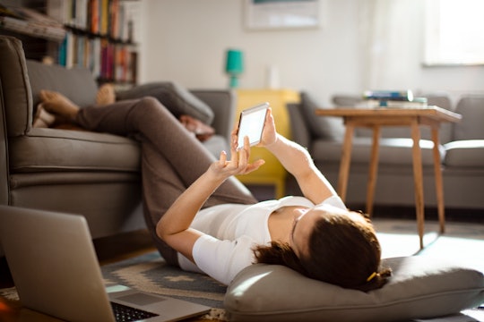 woman lying down in living room, looking at her phone
