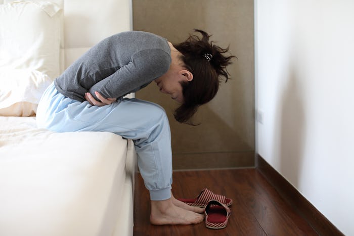 woman with cramps sitting on edge of bed