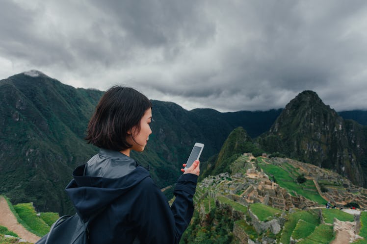A young woman stands in front of Machu Picchu with her phone in her hand.