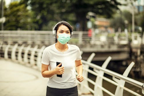 A person jogs outside with a mask on. You can exercise outside safely during the pandemic, as long a...