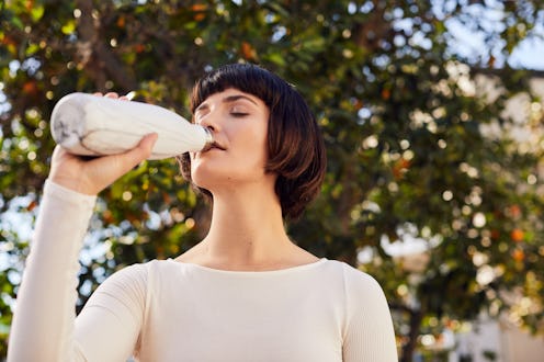 A woman drinks from a reusable water bottle. Drinking too much water? These are signs to look out fo...