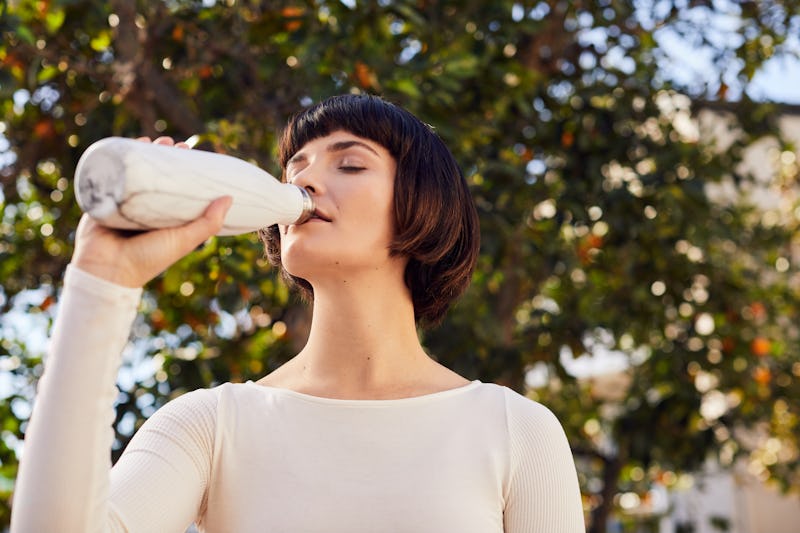 A woman drinks from a reusable water bottle. Drinking too much water? These are signs to look out fo...