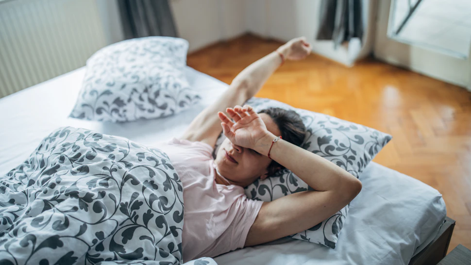 A person wearing a nightshirt and robe sits up in bed, stretching. If you're having trouble getting out of bed during COVID-19, you can still get in exercises that will help you feel a bit better.