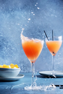Two bellinis are places on a table with a bowl of peaches next to them.
