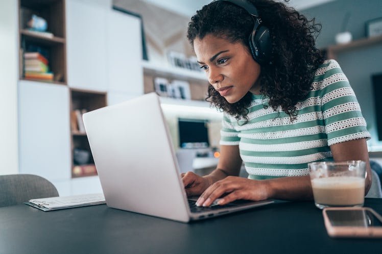 A young woman stares at her computer screen while wearing a pair of headphones.