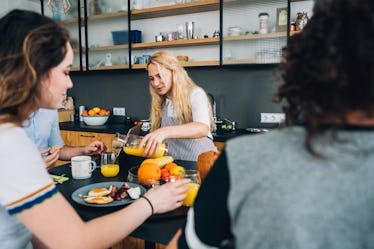 A blonde woman pours orange juice into her glass at a table with her family.