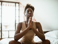 A yoga woman meditates while sitting on her bed in the morning.
