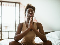 A yoga woman meditates while sitting on her bed in the morning.
