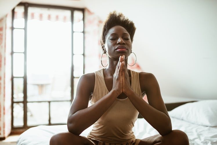 A yoga woman meditates while sitting on her bed in the morning.