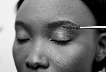 A close-up of a woman's face with closed eyes, while her eyebrows are being brushed into a proper sh...