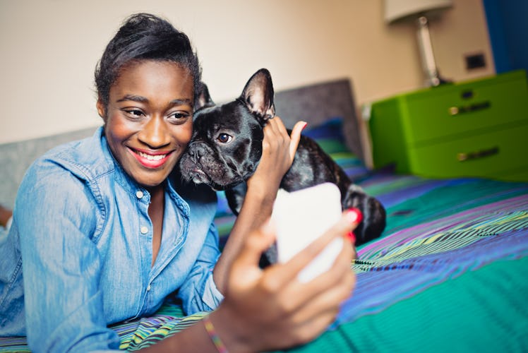 A young woman poses for a selfie with her puppy on a colorful bed.
