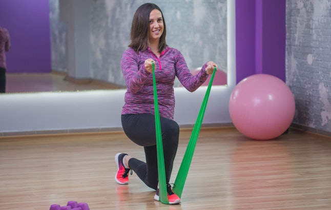 A person performs a half-kneeling bicep curl with a resistance band. You can workout at home to benefit every part of your body with only resistance bands.