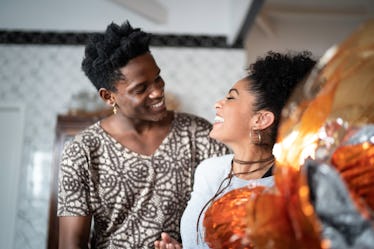 A trendy couple laughs in their kitchen while the girl holds a big wrapped Easter egg.